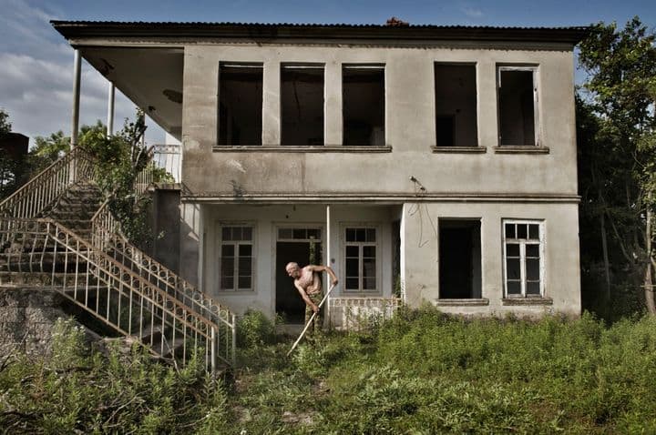 Abchazas šienauja žolę prie apleisto namo, kuriame gyveno gruzinų šeima. Nuotr. Yuri Kozyrev | Time